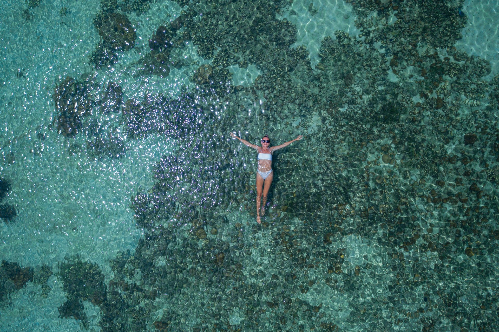 Aerial drone top view of woman floating in crystal clear sea water with coral reef